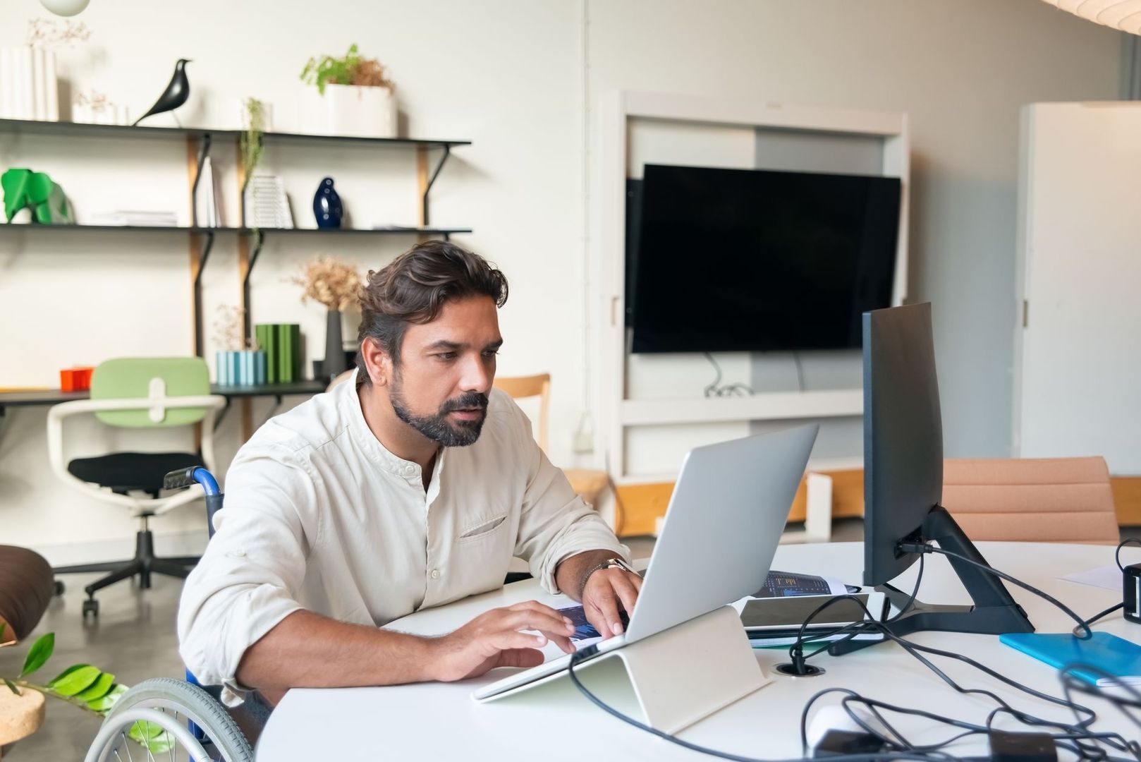 Man i rullstol arbetar vid laptop och bildskärm på kontor